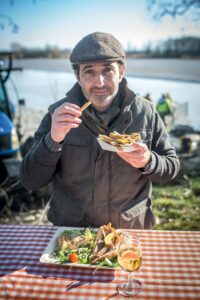 Homme qui déguste un cornet de goujonnette de carpe des Dombes et rillette de carpe des Dombes devant l'étang de la Dombes dans l'Ain