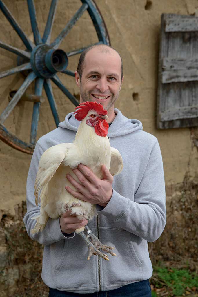 Cyrille Degluaire, éleveur devant une ferme tenant un chapon, photo présentée au Salon Agriculture 2018
