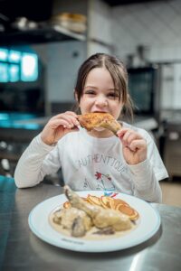 Jeune fille qui mord à pleine dent une cuisse de poulet de bresse au Restaurant La Table Bagesienne à Bâgé le Châtel.