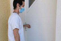 Un Infirmier du Département de l'Ain portant un masque qui frappe à la porte d'entrée d'un patient