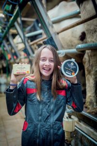 Jeune fille souriante tenant dans une main un pot de crème fraîche de Bresse et de l'autre un plaquette de beurre de la laiterie du Coq d'Or à Foissiat